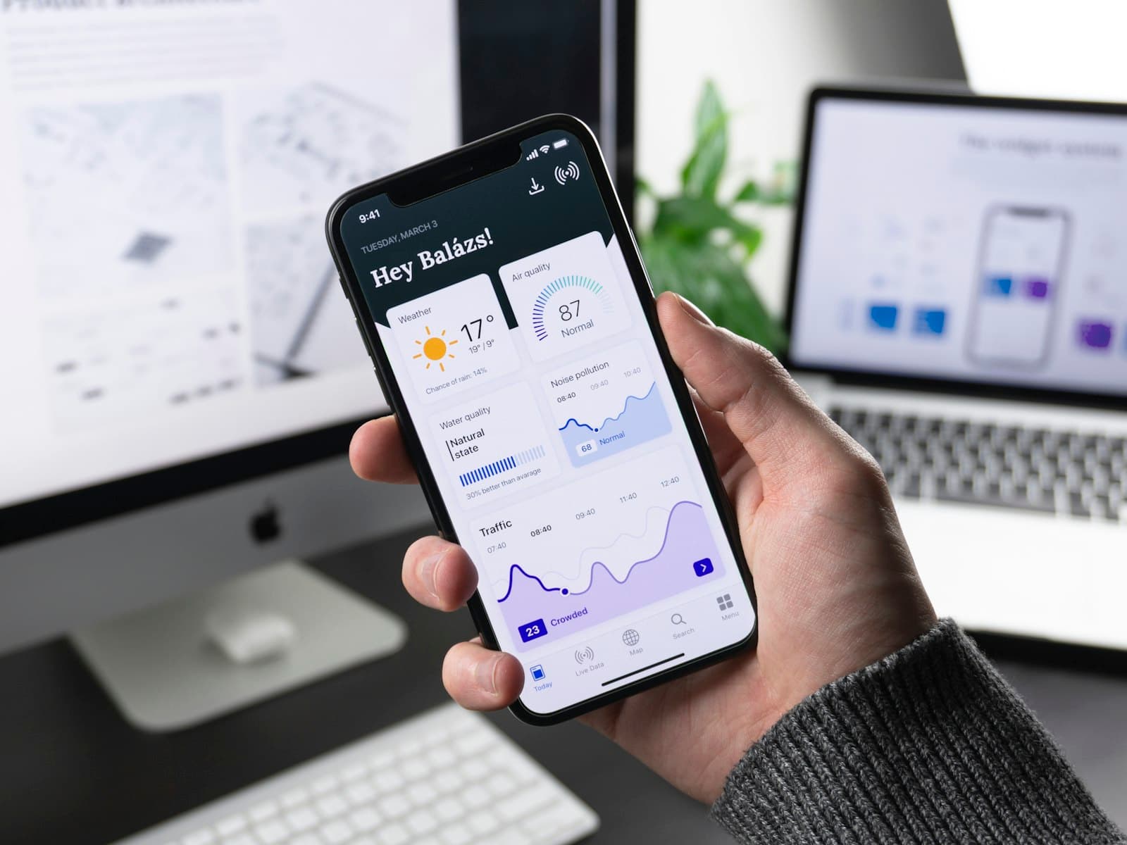A hand holding a phone that shows a dashboard of weather, air, and traffic.