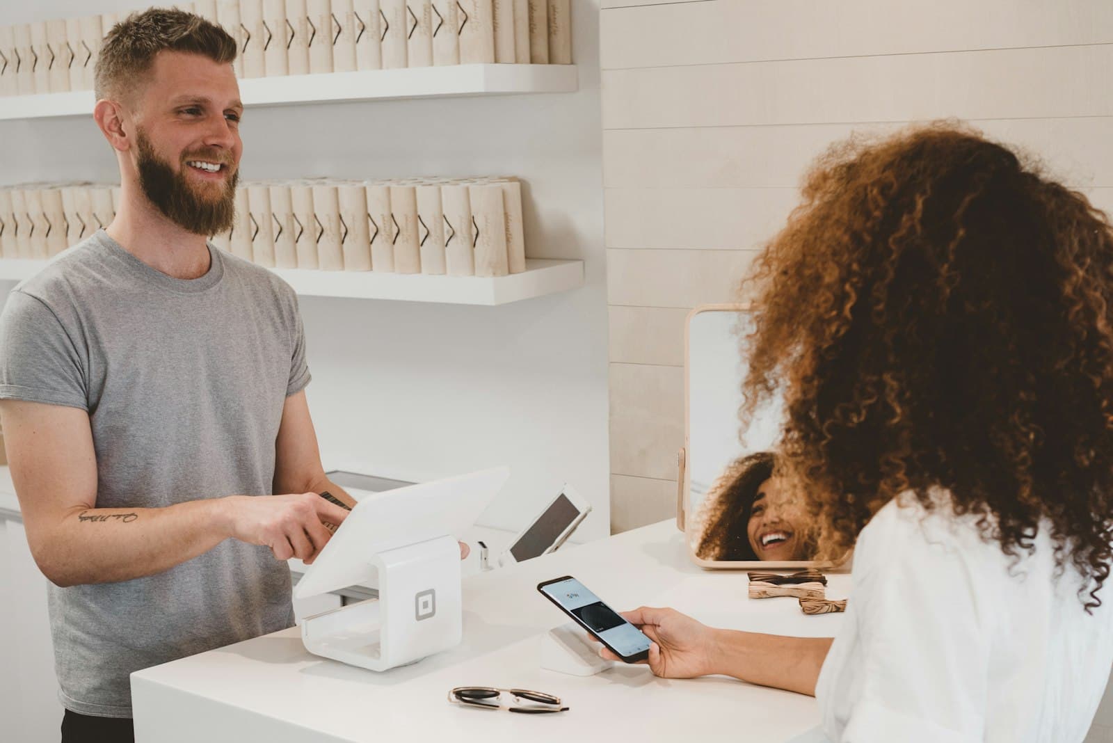 A customer paying by phone at a shop counter while a person works the register.