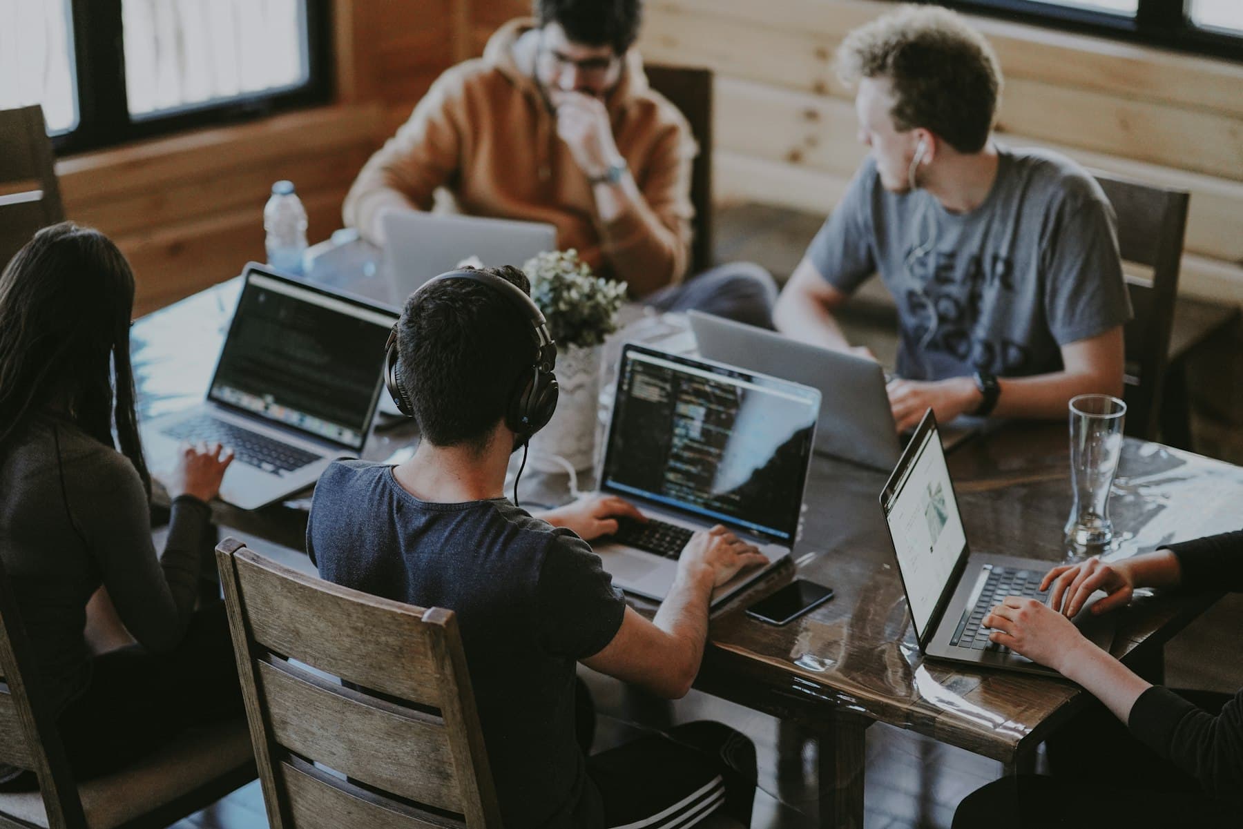 People working on laptops around a wooden table.